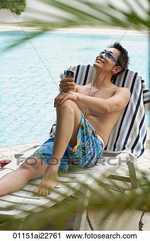 Stock Image - Man on deck chair listening to music. Fotosearch