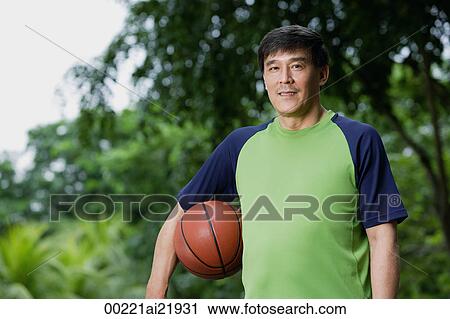 Stock Image - Man playing basketball, holding ball, in park. Fotosearch