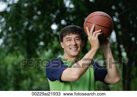 Stock Image - Man playing basketball in park, looking at camera, smiling. Fotosearch