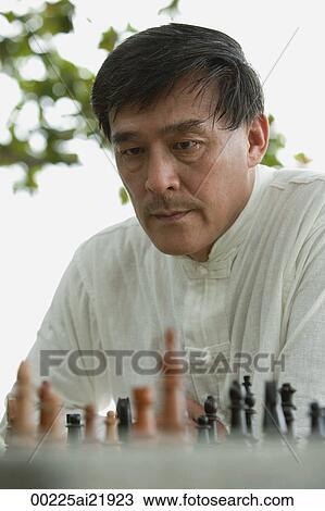 Stock Image - Man playing chess in park, deciding what move to make. Fotosearch