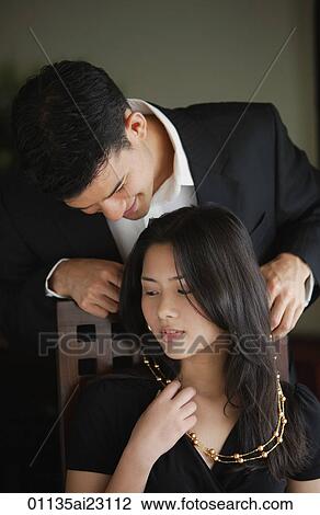 Stock Image - Man putting necklace around woman's neck. Fotosearch