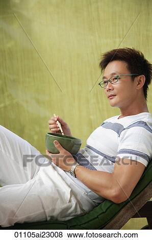 Man relaxing on deck chair while eating View Large Photo Image Stock Photo - Man relaxing on deck chair while eating. Fotosearch