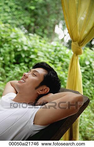 Stock Photograph - Man relaxing on lounge chair, outside. Fotosearch