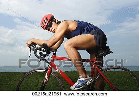 Stock Image - Man riding bike along ocean, looking at camera. Fotosearch