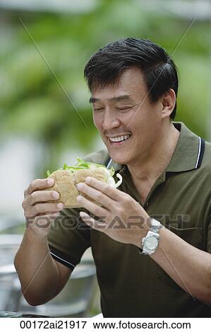 Man sitting in outdoor cafe eating sandwich View Large Photo Image Stock Photo - Man sitting in outdoor cafe eating sandwich. Fotosearch
