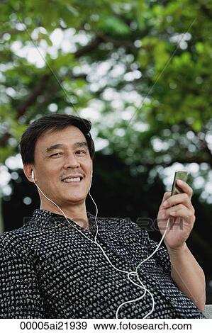 Man sitting in park listening to MP3 player, smiling View Large Photo Image Stock Photo - Man sitting in park listening to MP3 player, smiling. Fotosearch