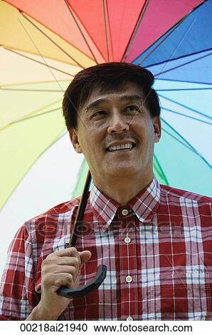 Man standing under rainbow umbrella, smiling View Large Photo Image Stock Image - Man standing under rainbow umbrella, smiling. Fotosearch