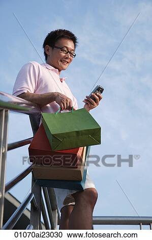 Stock Image - Man with shopping bags using mobile phone. Fotosearch
