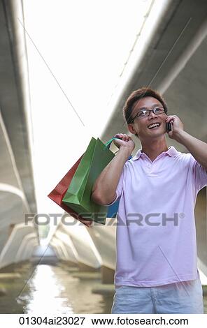 Stock Photo - Man with shopping bags using mobile phone. Fotosearch