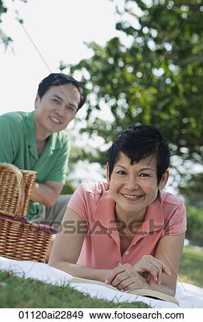 Stock Photo - Mature couple having a picnic in the park, smiling at camera. Fotosearch