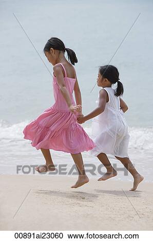 Stock Image - Sisters running on the beach and holding hands. Fotosearch