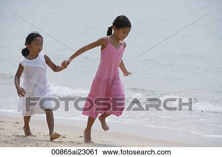 Stock Image - Sisters running while holding hands at the beach. Fotosearch