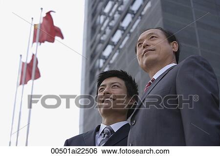 Stock Photograph - Two businessmen stand in front of a building with flags. Fotosearch