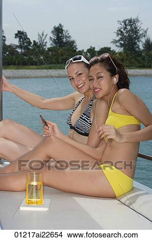 Picture - Two young women on a yacht, smiling at the camera. Fotosearch