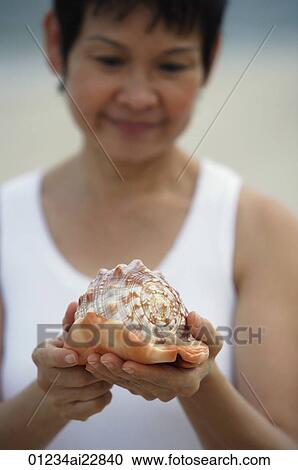 Stock Image - Woman at the beach holding a sea shell. Fotosearch