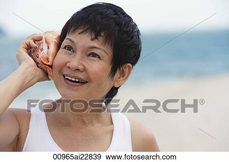 Stock Photo - Woman at the beach listening to sea shell. Fotosearch