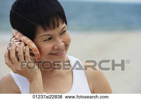 Woman at the beach listening to sea shell View Large Photo Image Stock Photo - Woman at the beach listening to sea shell. Fotosearch