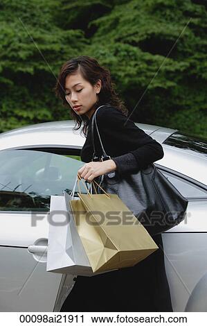 Stock Image - Woman carrying shopping bags and getting into car. Fotosearch
