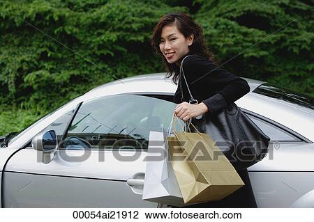 Stock Image - Woman carrying shopping bags, smiling at camera, getting into car. Fotosearch
