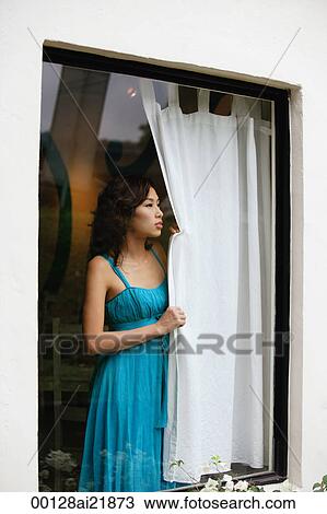 Woman looking out window, holding curtain, wearing dress View Large Photo Image Stock Image - Woman looking out window, holding curtain, wearing dress. Fotosearch