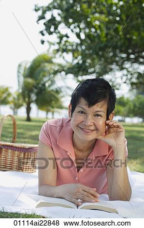 Stock Photo - Woman lying in the park, having a picnic. Fotosearch