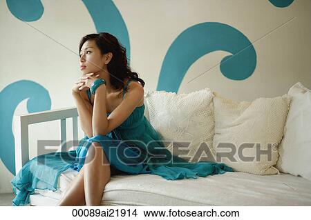 Picture - Woman sitting on daybed, looking away from camera. Fotosearch