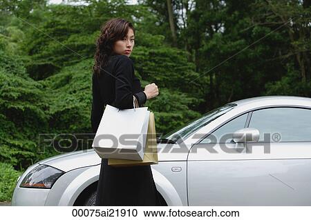 Woman walking to car, carrying shopping bags, looking over shoulder at camera View Large Photo Image Stock Image - Woman walking to car, carrying shopping bags, looking over shoulder at camera. Fotosearch