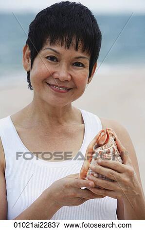 Woman with sea shell at the beach, smiling at camera View Large Photo Image Stock Photo - Woman with sea shell at the beach, smiling at camera. Fotosearch