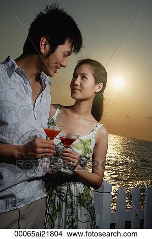 Picture - Young couple on beach at sunset with martini drinks. Fotosearch