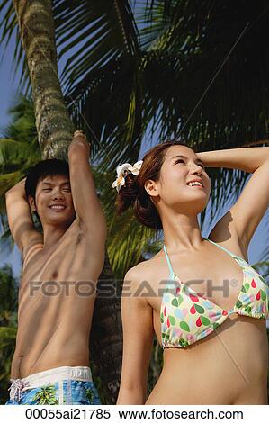 Stock Photography - Young couple on beach by palm tree. Fotosearch