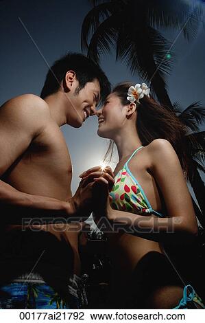 Stock Image - Young couple on beach holding hands and smiling at each other. Fotosearch