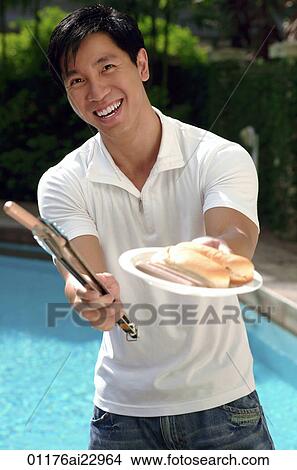 Young man offering hot dog and smiling at camera View Large Photo Image Picture - Young man offering hot dog and smiling at camera. Fotosearch