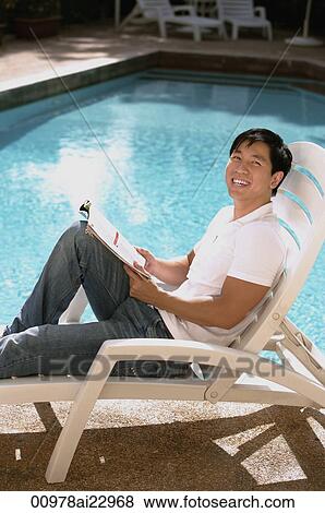 Young man relaxing in deck chair by the pool View Large Photo Image Stock Photo - Young man relaxing in deck chair by the pool. Fotosearch