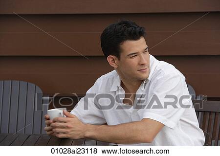 Young man sitting at table looking over his shoulder View Large Photo Image Stock Photo - Young man sitting at table looking over his shoulder. Fotosearch