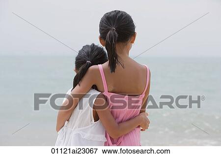 Stock Photo - Young sisters hugging and looking out at sea. Fotosearch