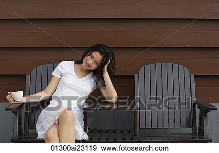 Stock Photo - Young woman enjoying cup of tea in garden chair. Fotosearch