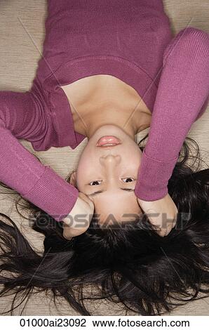 Stock Image - Young woman looking upside down at camera. Fotosearch