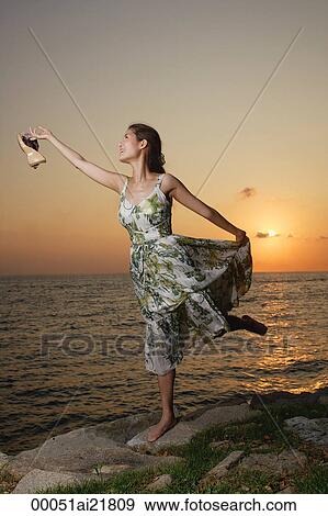 Stock Photo - Young woman walking along rocks on beach. Fotosearch