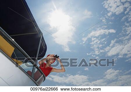 Stock Photograph - Young woman with binoculars on yacht, looking into distance. Fotosearch