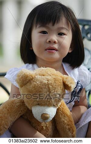 Stock Image - A young girl looking at camera, holding teddy bear. Fotosearch