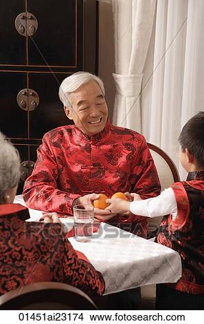 Boy presenting two mandarin oranges to grandfather at dinner table View Large Photo Image Picture - Boy presenting two mandarin oranges to grandfather at dinner table. Fotosearch