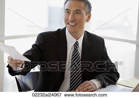 Stock Photo - businessman at table, holding papers. Fotosearch