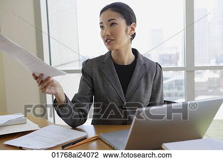 Stock Image - businesswoman at desk, holding papers. Fotosearch