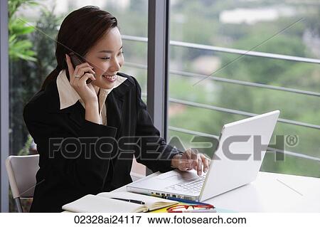 Stock Photo - businesswoman at laptop with cell phone. Fotosearch