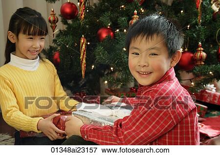 Children with presents sitting under Christmas tree, boy looking at camera View Large Photo Image Stock Photo - Children with presents sitting under Christmas tree, boy looking at camera. Fotosearch