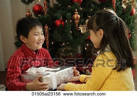 Stock Photograph - Children with presents sitting under Christmas tree. Fotosearch