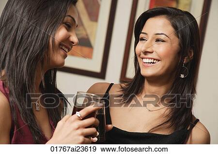 Stock Photo - close up of two women talking, drinks in hand. Fotosearch