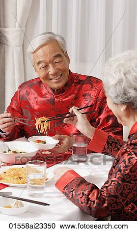 Stock Image - Elderly couple in traditional clothing at dinner table. Fotosearch