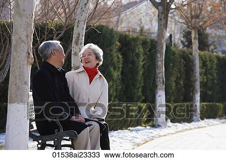Stock Image - Elderly couple sitting on park bench. Fotosearch