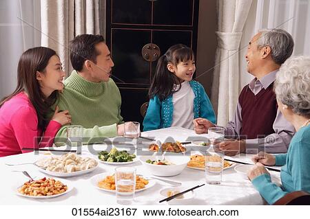 Family at dinner table having traditional food, girl standing next to grandfather View Large Photo Image Stock Photo - Family at dinner table having traditional food, girl standing next to grandfather. Fotosearch